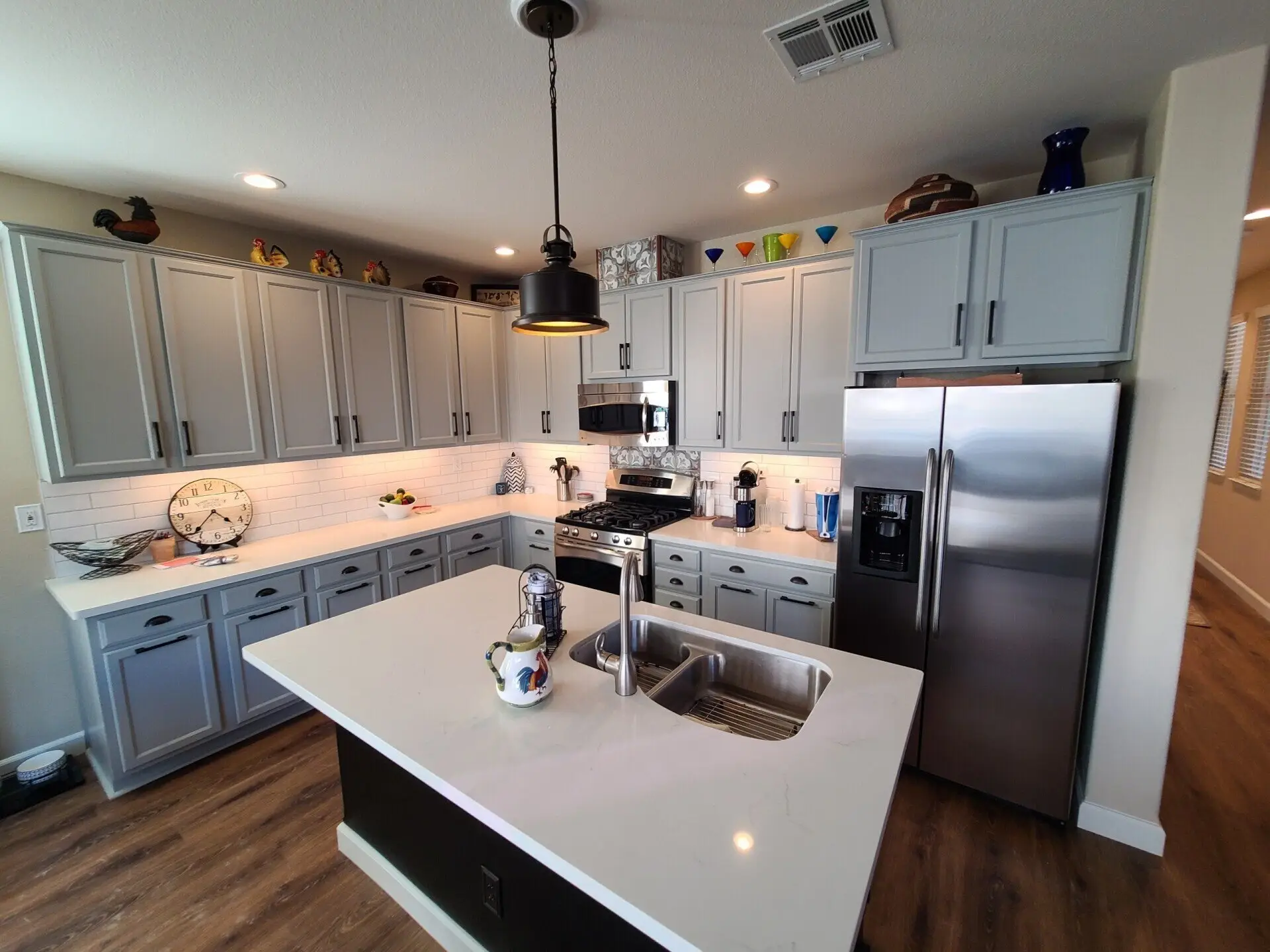 Kitchen cabinets repainted light grey with black pulls, white quartz counters and a dark island