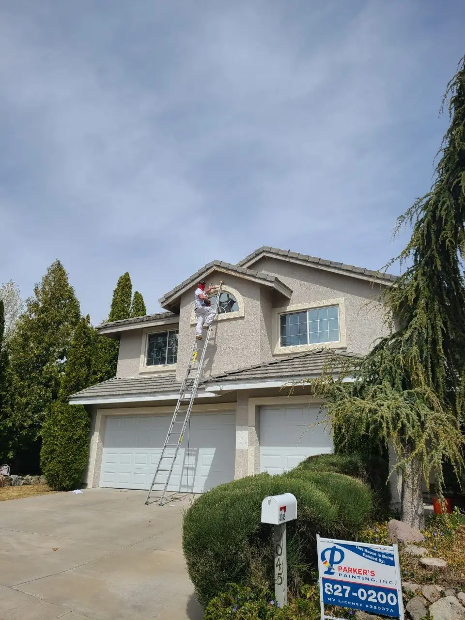 Parker’s Painting crew member on a ladder painting the trim of a two-storey stucco home